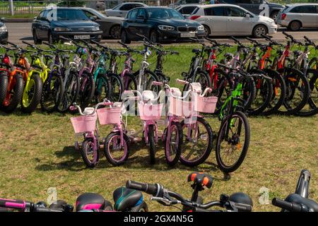 Pinke Kinderfahrräder stehen an einem Sommertag zum Verkauf und zur Miete auf dem Rasen vor den Autos zur Verfügung. Stockfoto