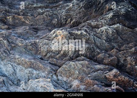 Nahaufnahme einer rauen und rauen Felsoberfläche. Sieht aus wie eine zerklüftete Landschaft von oben. Abstrakter, natürlicher strukturierter Hintergrund. Stockfoto