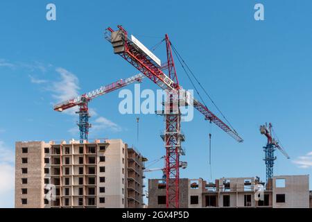 Turmdrehkrane arbeiten am Bau von gemauerten Wohngebäuden vor dem Hintergrund eines blauen Himmels. Stockfoto