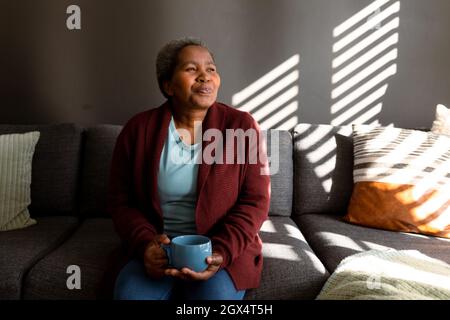 Entspannte afroamerikanische ältere Frau, die auf dem Sofa sitzt und Kaffee trinkt Stockfoto