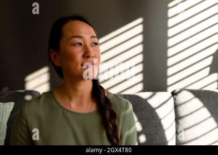 Porträt einer lächelnden asiatischen Frau, die zu Hause auf dem Sofa sitzt Stockfoto