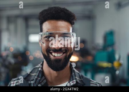 Porträt eines glücklichen jungen Industriemannes, der in einer Metallwerkstatt arbeitet und die Kamera anschaut. Stockfoto