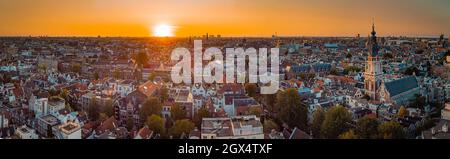 Schönes Abendpanorama der Stadt Amstedam mit Blick nach Westen mit wunderschönem Sonnenuntergang und Sonnenuntergang über Amsterdam. Drohnenansicht. Stockfoto