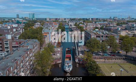 Luftdrohnenaufnahme eines Schiffes, das an einer hochgelegenen Straßenbrücke im amsterdamer Kanal vorbeifährt. Schiff unter offener Brücke über den Kanal. Stockfoto