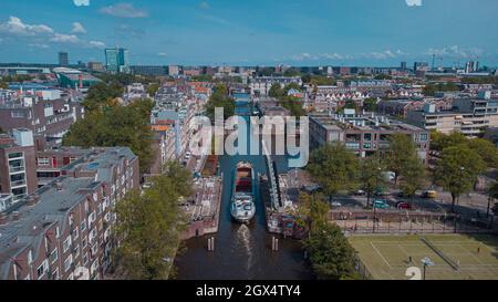 Luftdrohnenaufnahme eines Schiffes, das an einer hochgelegenen Straßenbrücke im amsterdamer Kanal vorbeifährt. Schiff unter offener Brücke über den Kanal. Stockfoto