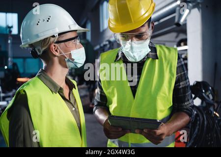 Portrait von Industrieinspektoren mit Gesichtsmasken, die in Innenräumen in der Metallwerkstatt eine allgemeine Überprüfung durchführen, Coronavirus-Konzept. Stockfoto