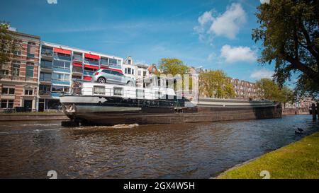 Blick auf ein Schiff, das über eine aufragende Straßenbrücke im amsterdamer Kanal fährt. Schiff unter offener Brücke über den Kanal. Stockfoto