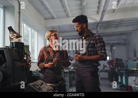 Portrait von jungen biracial Industriekollegen, die sich in einer Metallwerkstatt unterhalten. Stockfoto