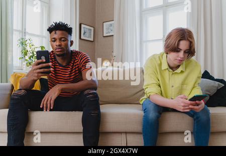 Junge Biracial Paar süchtig nach Smartphones sitzen auf dem Sofa zu Hause, Social-Media-Konzept. Stockfoto