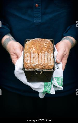 Mann, der ein hausgemachtes Brot aus frisch gebackenem Dinkel-Vollkornsoda in einer Dose hält Stockfoto