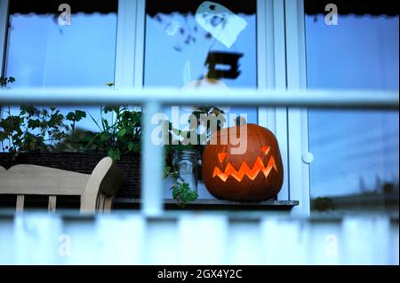 Ein traditioneller Halloween Jack Lantern Kürbis, der hinter einem Fenster steht. Stockfoto