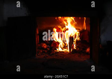 Unschärfe-Effekte im Hintergrund der Feuerflamme. Brennendes Brennholz im alten Ofen oder Ofen. Dunkel und schwarz. Orangefarbene Flamme. Wärmeenergie. Öffnen Sie die Eisentür. Nicht fokussiert. Stockfoto