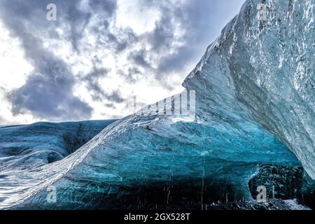 Der Überhang einer Eishöhle in Island. Die Höhlen sind in Blautönen gefärbt und haben oft schwarze Schichten, die aus vulkanischer Asche gebildet werden. Stockfoto