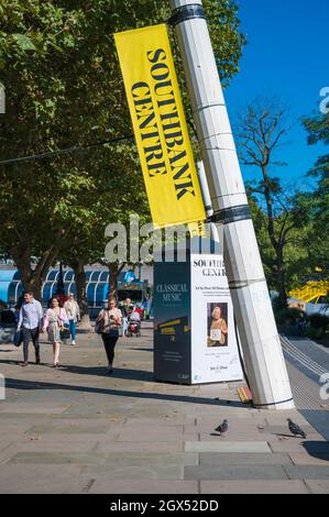 Leute, die an einem sonnigen Tag spazieren, kommen an einem Kiosk mit Werbetafeln vorbei, auf denen Kunst- und Musikveranstaltungen im Southbank Center angezeigt werden. London, England, Großbritannien Stockfoto