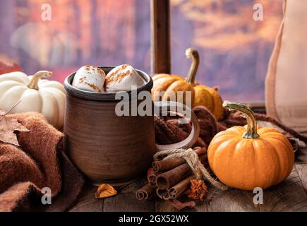 Tasse heiße Schokolade mit Salmellchen und Kürbissen auf einem Holztisch an einem Fenster mit herbstlichem Hintergrund Stockfoto