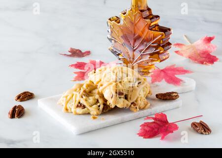 Ein kleiner Stapel Pekannüsse aus Ahorn auf einer Marmorplatte mit einer Flasche Ahornsirup dahinter. Stockfoto