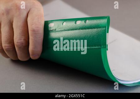 Ein erwachsener Mann hält einen grünen Ordner in seiner rechten Hand. Person mit einem Finanzbericht oder Geschäftsprojekt auf grauer Oberfläche. Nahaufnahme. Sele Stockfoto
