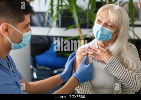 Ältere Dame, Die Gegen Covid Geimpft Wird, Arzt, Der Eine Klebende Bandage Anwendet Stockfoto