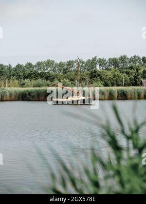 Eine Segelyacht im traditionellen Stil, die sicher auf einer breiten Landschaft in Horsey auf den Norfolk Broads, Norfolk England, Großbritannien, festgemacht ist Stockfoto