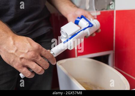 Austausch von Teilen des Toilettentanks. Ein Mann in orangefarbenen Handschuhen repariert den Abfluss des Toilettenbehälters Stockfoto