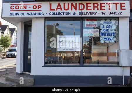 Oktober 2021. Außenansicht einer Münzwaschanlage an einer Straßenecke in Southend-on-Sea, Großbritannien. Beschilderung wirbt für Service Waschen, Abholen und Lieferung, Bügeln und Bettreinigung. Im Fenster ist ein gedruckter Hinweis neben Werbeschildern im Neonstil zu sehen. Eine seit langem etablierte Waschanlage war aufgrund des anhaltenden Anstiegs der Energiepreise und der wirtschaftlichen Auswirkungen der covid-Pandemie gezwungen, ihre Türen zu schließen. Penelope Barritt/Alamy Live News Stockfoto
