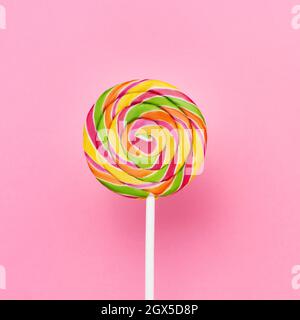 Regenbogen-Lollipop wirbeln auf einem weißen Stock über rosa Hintergrund. Draufsicht, Platz für Text kopieren Stockfoto