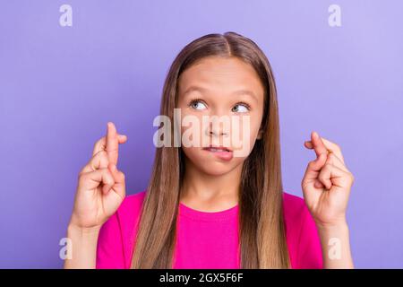 Foto von jungen gesinnten neugierigen kleinen Mädchen suchen leeren Raum gekreuzte Finger isoliert auf lila Hintergrund Stockfoto