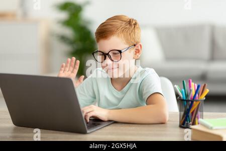 Fröhlicher Rotschopf Kid Nerd mit Videoanruf mit Tutor Stockfoto