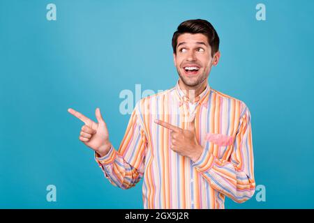 Foto von jungen aufgeregt Mann glücklich positive Lächeln zeigen Finger leeren Raum wählen promo isoliert über blauen Hintergrund Stockfoto