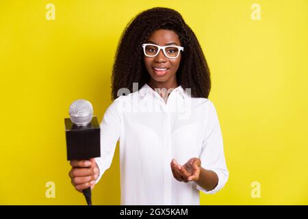 Fotoportrait einer Reporterin, die Interviews mit einem Mikrofon nimmt, das einen lebhaften gelben Hintergrund isoliert Stockfoto