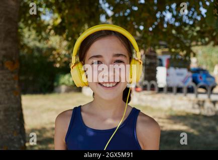 Nahaufnahme eines wunderschönen spanischen Mädchens, das lächelt und zur Kamera schaut und gelbe Kopfhörer verwendet. Ein schönes spanisches Mädchen schaut zur Kamera, während Stockfoto