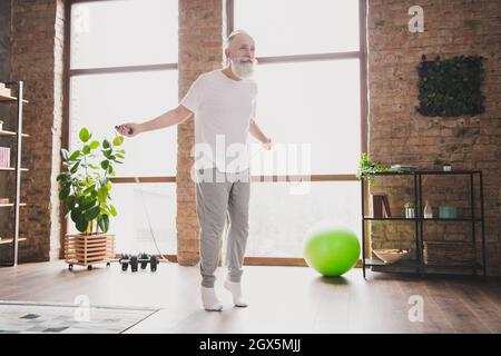 Foto in voller Größe des glücklichen positiv lächelnden Großvaters, der mit einem Seilspringen im Haus mit Herz springt Stockfoto