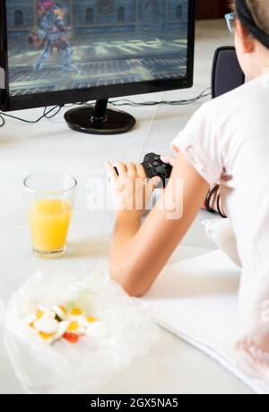 Unbekanntes kleines Mädchen spielt Videospiel und trinkt Saft zu Hause Stockfoto