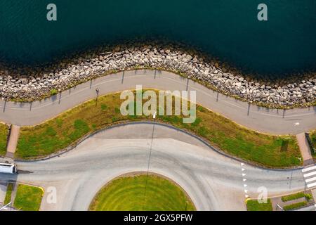 Von oben Böschung mit Asphaltweg und Rasen zwischen ruhigem Wasser und Kreisverkehr Straße am Sommertag in der Küstenstadt gelegen. Stockfoto