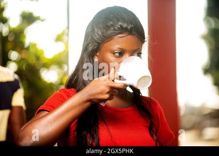 Porträt einer schönen Frau, die beim Lächeln eine Tasse Kaffee in der Nähe eines Restaurants trinkt Stockfoto