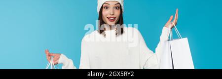 Aufgeregte Frau in warmer Kleidung, die Einkaufstaschen isoliert auf blauem Banner hält Stockfoto