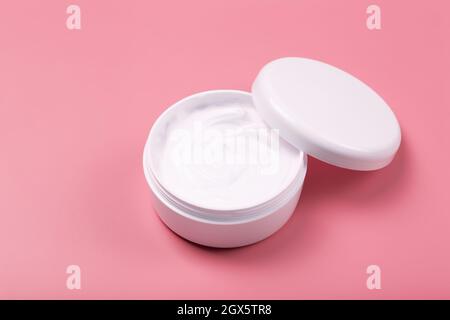 Kosmetische Creme Hintergrund. Weiße kosmetische Creme für Haut und Körper in einem offenen weißen Glas auf einem rosafarbenen leeren Hintergrund. Hochwertige Fotos Stockfoto