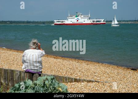 Lady saß an der Meereswand und beobachtete die Red Funnel Ferry, Calshot Beach, Calshot, Hampshire, Großbritannien. Stockfoto