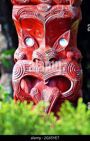 Ein roter hölzerner Maori tekoteko mit einer hervorstehenden Zunge und Augen von Paua-Muscheln steht 2005 in Rotorua, Neuseeland. Das Erzählen von Geschichten durch Holzhandwerk ist eine Tradition der Maori, wobei jeder Tekoteko eine einzigartige Geschichte erzählt. Stockfoto