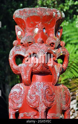 Ein roter hölzerner Maori tekoteko mit einer hervorstehenden Zunge und Augen von Paua-Muscheln steht 2005 in Rotorua, Neuseeland. Das Erzählen von Geschichten durch Holzhandwerk ist eine Tradition der Maori, wobei jeder Tekoteko eine einzigartige Geschichte erzählt. Stockfoto