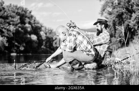 Männer sitzen am Flussufer mit Angelausrüstung. Wilderei Kriminalität und Angelschein. Wilderer, die fischen. Schwarzmarkt Kaviar. Illegale Jagd Kaviar Stockfoto