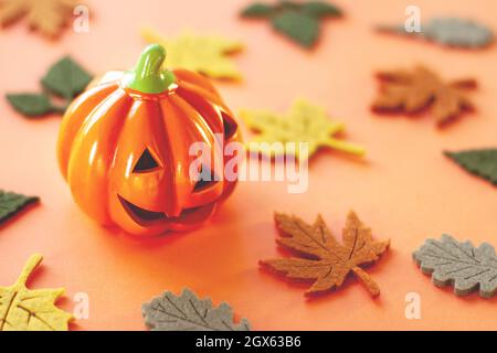 Deko orange kleines Lächeln Halloween Kürbis mit Herbst Ahorn Eiche Filzblätter von gelb rot braun und grün Farben in der Nähe auf orangefarbenem Hintergrund und Stockfoto