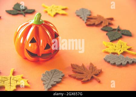 Deko orange kleines Lächeln Halloween Kürbis mit Herbst Ahorn Eiche Filzblätter von gelb rot braun und grün Farben in der Nähe auf orangefarbenem Hintergrund und Stockfoto
