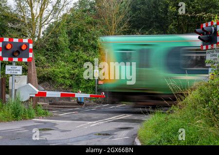 Zug über einen automatischen halben Barriere Bahnübergang auf der Südbahn in West sussex uk. Bahnübergang auf der Bahn mit Straßensperren. Stockfoto