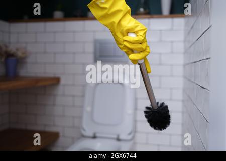 Reiniger in gelben Gummihandschuhen, die die Toilettenbürste in Nahaufnahme halten Stockfoto