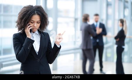 Schwarze Geschäftsfrau, die im Bürogebäude telefoniert, Mitarbeiter im Hintergrund Stockfoto