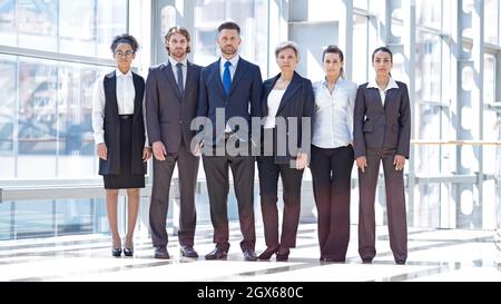 Multiethnische Gruppe von selbstbewussten Geschäftsleuten in formeller Kleidung Team drinnen modernes Gebäude in voller Länge Porträt Stockfoto