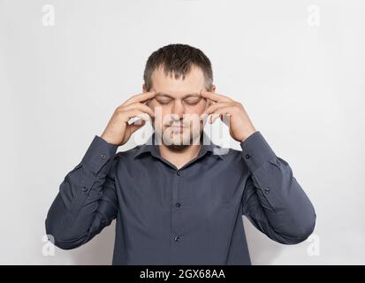 Ein 30-jähriger Mann hält seine Hände auf weißem Grund an seinen Schläfen. Stockfoto