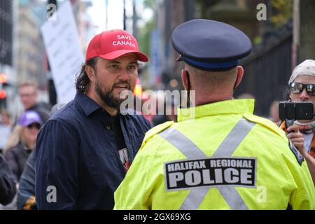 Halifax, Nova Scotia, Kanada. 4. Oktober 2021.Protestler, der vor der NS-Legislaturperiode mit der Polizei gegen den „Scotia Pass“-Protest (Impfmandat) argumentiert. Der Protestler trägt einen roten Hut „Save Canada“, der dem rechten US-Hut nachempfunden ist. Stockfoto