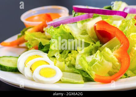 Salat mit einer Seite von vereierten Eiern. Auf einem Teller mit einer kleinen Tasse Dressing sitzen weiße und gelbe Eier. Daneben ist ein Salat gemacht Stockfoto